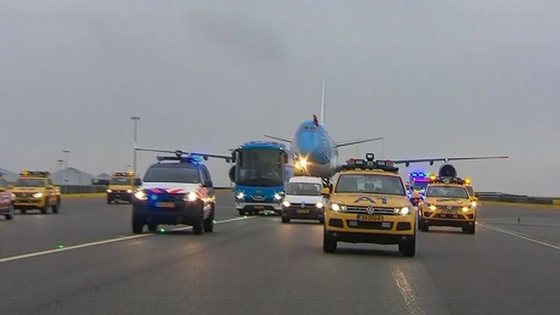 Het vliegtuig wordt op Schiphol door veel wagens begeleid.